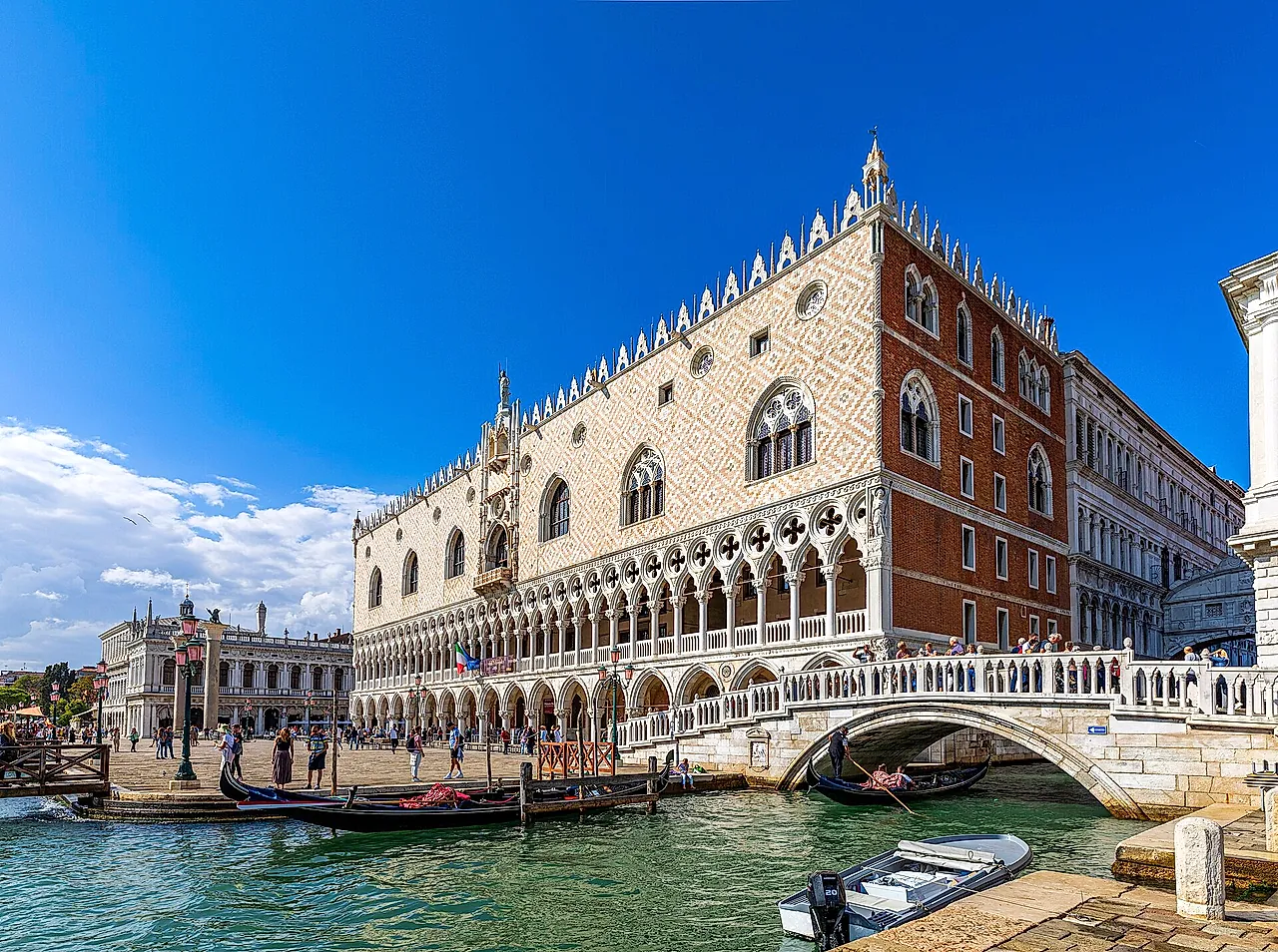 The corner of the Doge's Palace beside the canal and a stone bridge, with its pink and white walls and Gothic arcades