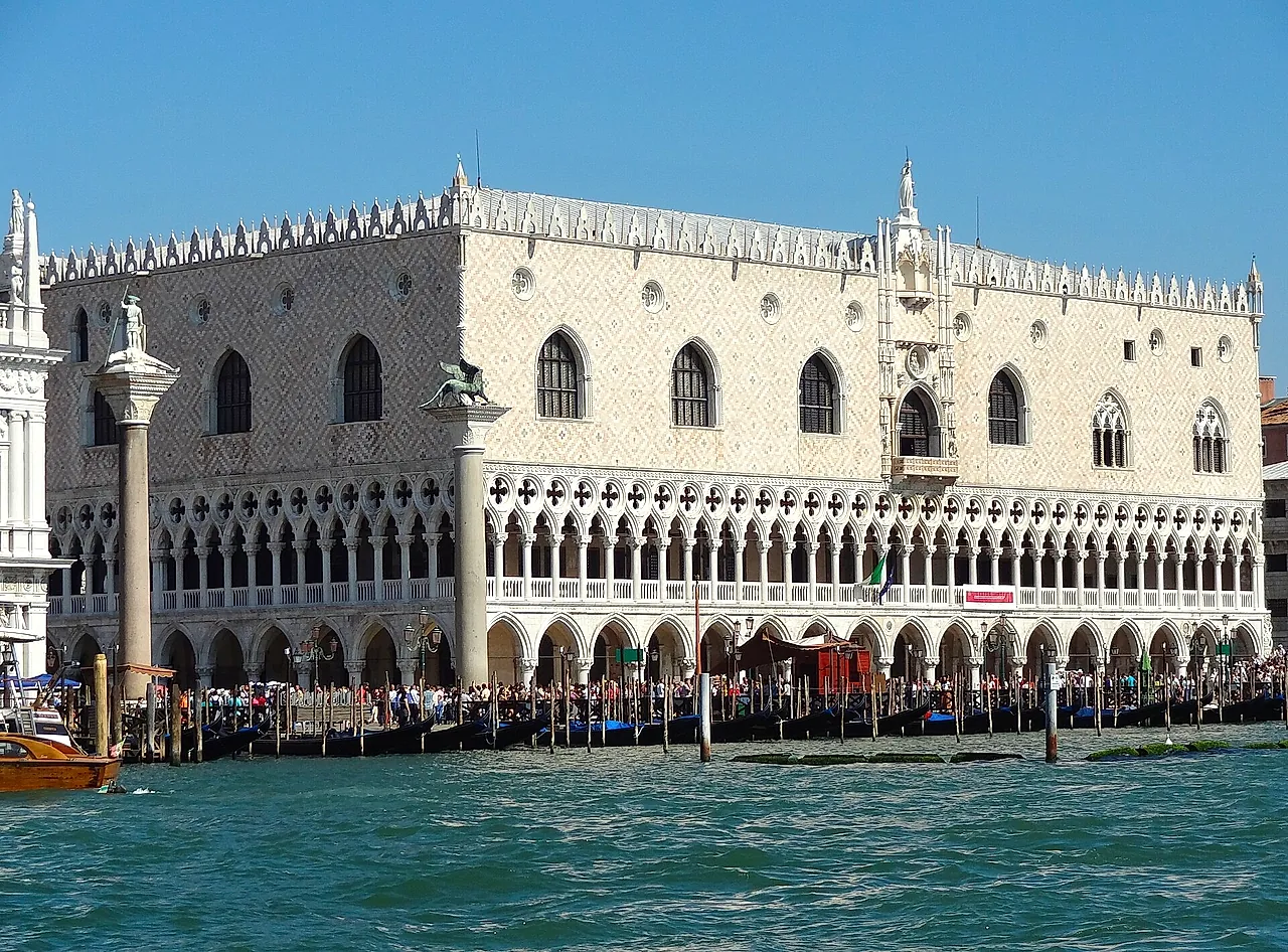 The Gothic façade of the Doge's Palace on the waterfront, with white arcades and a pink-and-white patterned wall under a blue sky