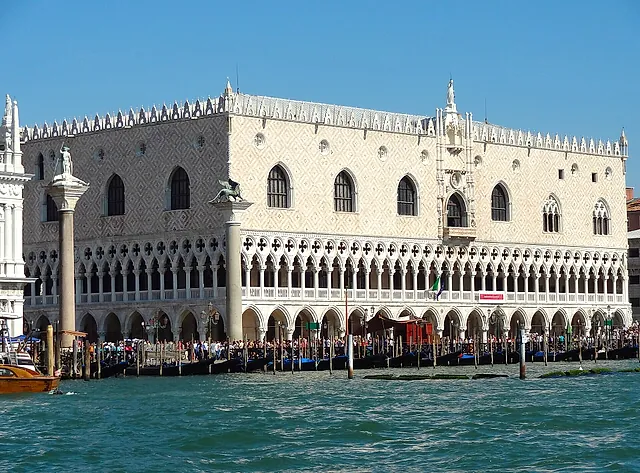 The Gothic façade of the Doge's Palace on the waterfront, with white arcades and a pink-and-white patterned wall under a blue sky