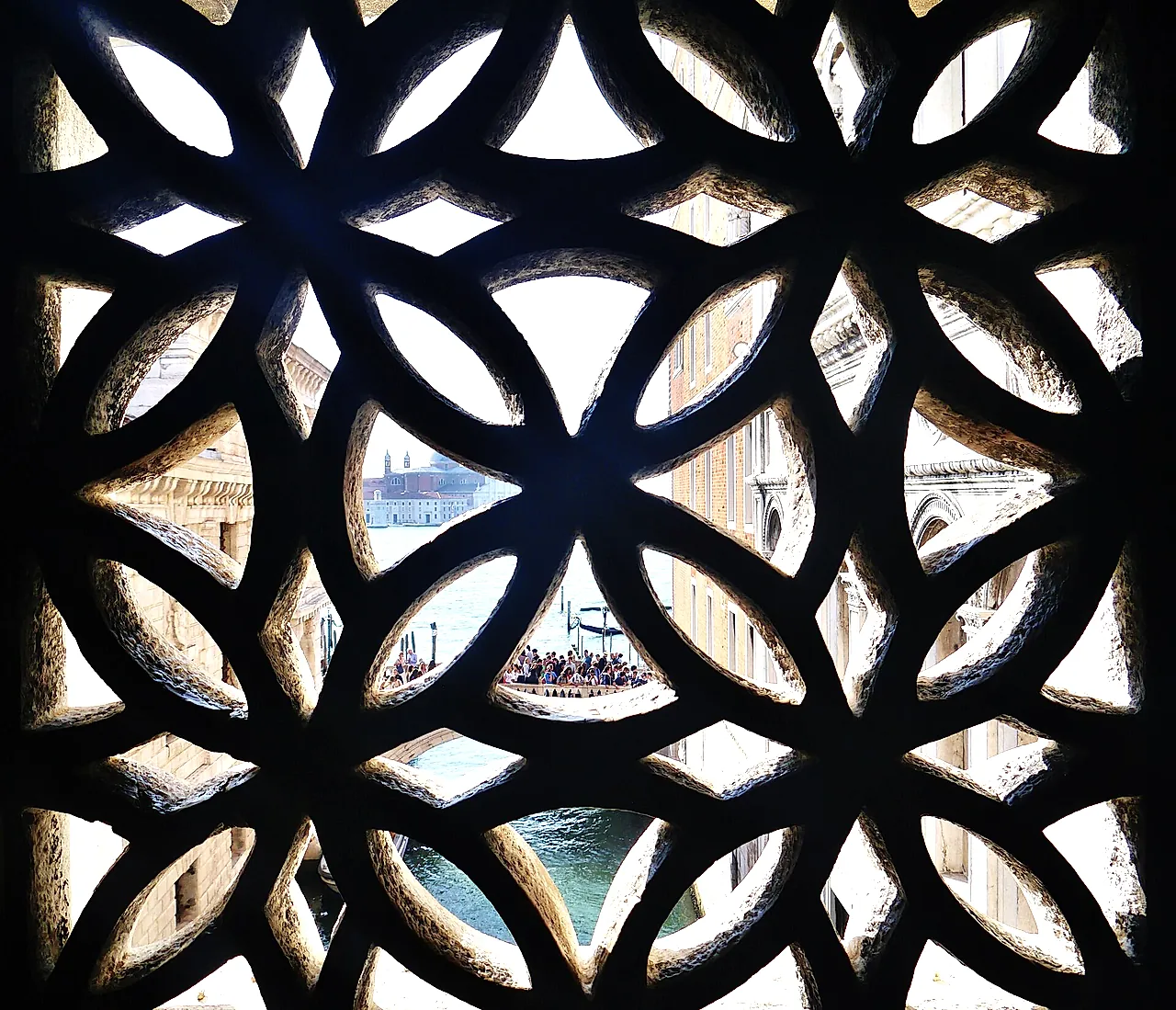 A stone-lattice window inside the Bridge of Sighs, with a glimpse of the lagoon beyond