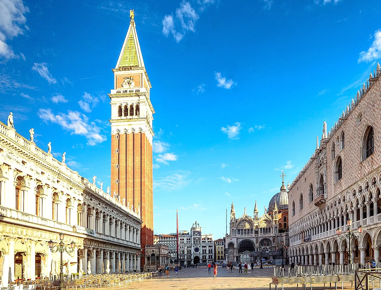 St Mark's Campanile rising above Piazza San Marco under a blue sky, with the Libreria Marciana and the Doge's Palace on either side