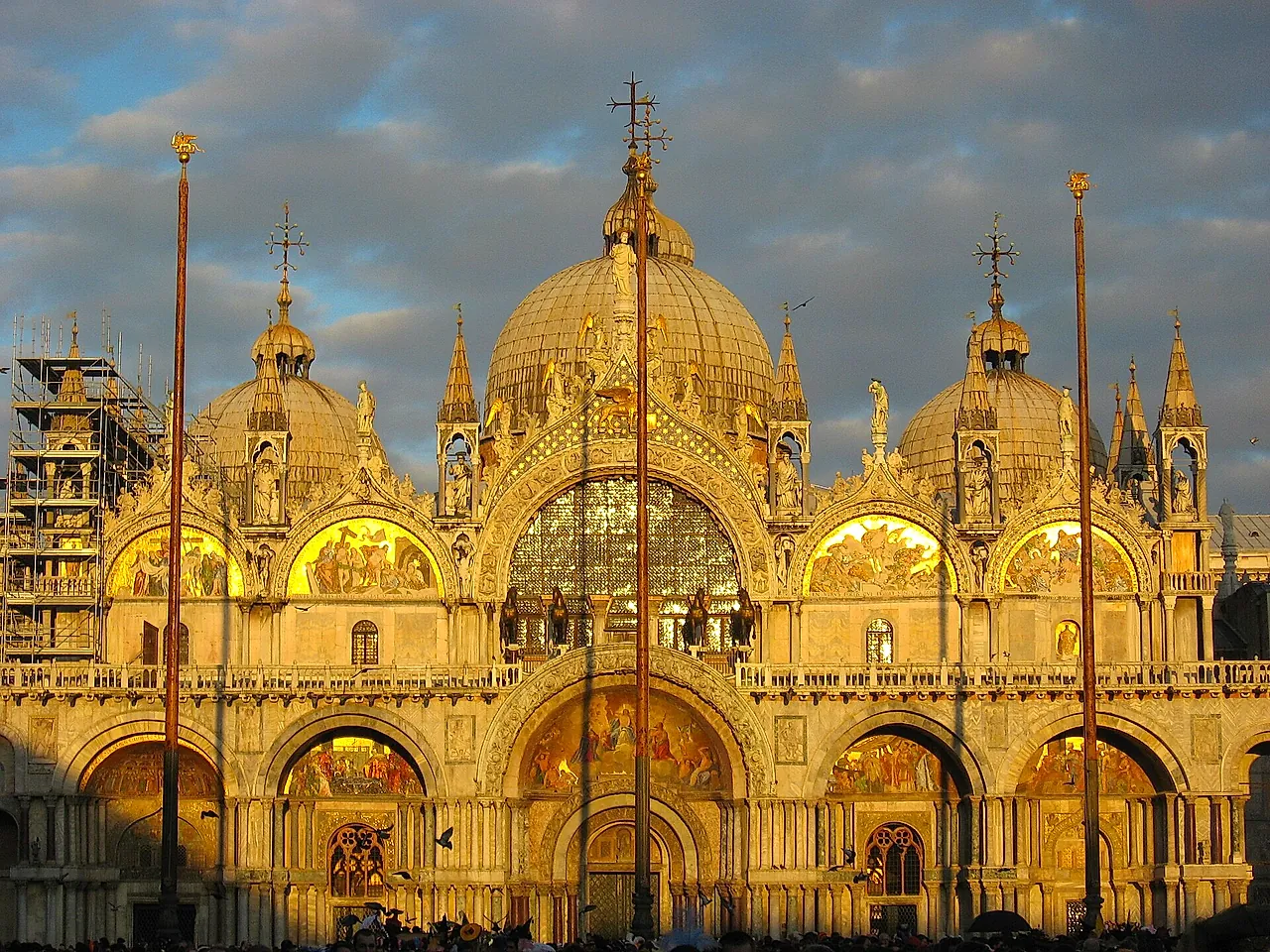 The west façade of St Mark's Basilica glowing in golden evening light, with its domes and mosaic lunettes
