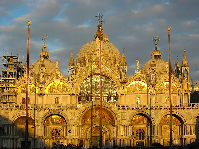 The west façade of St Mark's Basilica glowing in golden evening light, with its domes and mosaic lunettes